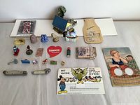Overview of assorted vintage miniature trinkets and collectibles including small figurines, pins, badges, novelty signs, and paper items on a flat surface.