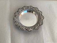 Top view showing round silver tray with scalloped raised edge and textured floral and scroll design