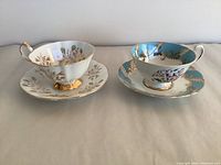 Pair of fine bone china tea cups and saucers, one set white with gold floral pattern (Paragon), one set blue with ornate gold and floral decoration (Queen Anne).