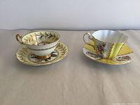 Two bone china tea cup and saucer sets placed side by side, one with yellow and floral gold leaf design, the other scalloped and yellow with floral sections.