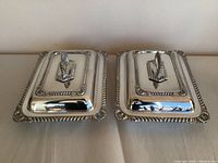 Pair of silverplated covered serving dishes with decorative edges and handles showing top view with lids on.
