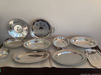 View of all 8 silverplated servingware pieces showing variety of shapes including trays, bowls, platters with some engraving and handles.