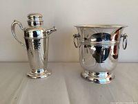 Photo of the hammered silverplated pitcher and the hotel style ice bucket side by side on a plain surface.