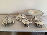 Photo showing all six silverplated servingware pieces including covered butter dish, covered cheese dish, pedestal cake stand, two covered serving dishes with handles, and a small serving tray.
