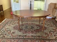 Full view of oval solid wood dining table in a room, showing shape, finish, and turned legs.