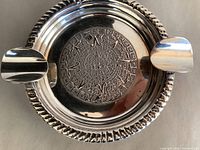 Close-up top view of round sterling silver ashtray showing detailed Aztec calendar design in center and two cigar rests.