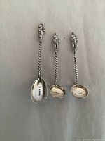Three antique sterling silver spoons with twisted handles and standing figure toppers displayed together to show full length and individual design differences.