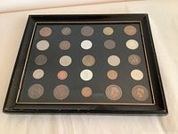Full view of the framed coin collection showing 25 coins arranged in five rows of five each. The frame is black with gold trim and measures about 12 by 10 inches.
