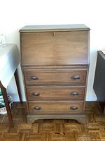 Front view of the closed secretary desk showing drop-front panel and three drawers with recessed handles.