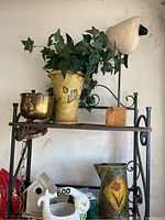 Full view of bakers rack 2 shelves with various decorative items including faux foliage sheep, brass bowl, and metal pitcher.