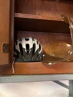 Silver and black bicycle helmet next to a brown plastic visor on a wooden shelf.