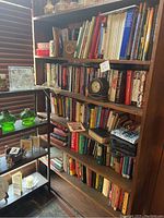 Bookshelves filled with a variety of books, small decorative green glass items on adjacent shelves, home decor items including glass and metal items
