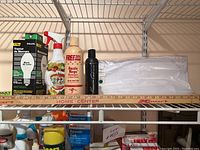 Shelf holding Philips light bulb, spray starch, black bottle, and stacked white pans