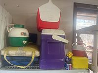 Coolers include green and white large cooler with tap, red and white cooler, purple cooler with crank handle, orange and white small cooler arranged on a metal shelf.