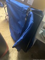 Blue fabric-covered display case or exhibit frame folded with attached strap, standing upright