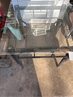 Top angled view of one square glass table showing clear glass surfaces and black metal frame.