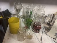 Photo of assorted clear and green antique glass lantern globes and shades, plus a small glass and metal heater/lantern item and juicer