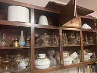 Multi-shelf cabinet with assorted oil lamp parts, chimneys, reservoirs, burners, and shades