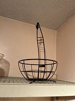 Black metal wire fruit basket with handle on shelf