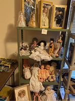 Full view of metal shelving unit filled with multiple dolls including unboxed and display dolls, some seated and some standing, with other boxed dolls on top shelf