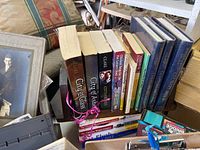 Books including 'City of Glass', culinary arts books and other titles grouped on shelf next to a wooden organizer and photo frame containing old portraits.