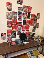 Wall display of multiple racing and matchbox cars in original packaging, arranged on a wall above a table with other car and airplane models and cases.