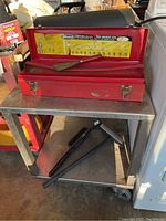 Close-up photo of red metal toolbox with Kobalt chrome alloy socket set inside, placed on metal table under one of the rolling carts. Hammer also seen.