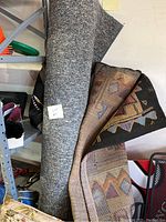 Photo showing two folded rugs with geometric patterns leaning on shelving.