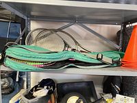 Photo showing green padded carrying case with multiple rackets inside plus orange sports cones on shelf above.