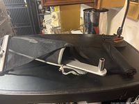 Folded metal arm accessory in black carrying bag on top of surface