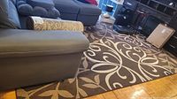Overall view of the nylon area rug in a room setting showing beige iron fleur pattern on dark brown background.
