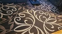 Full view of large brown area rug with cream Iron Fleur pattern near couch and chair.