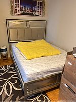 Full view of bed frame assembled with mattress and yellow bedding covering mattress surface to show scale and design.