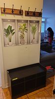 Photo of the entrance bench under three wall art pieces with two wall-mounted coat racks above it, showing overall setup and dimensions in room.