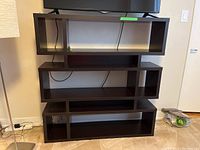 Photo of stacked dark brown cubby-style bookcase showing front and side views, placed on carpeted floor near wall, TV set on top shelf.