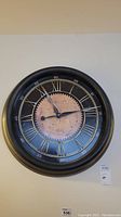 Front view of the 24-inch round wall clock featuring Roman numerals and antique map center design.