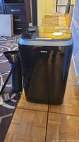 Front view of black Danby portable air conditioner with exhaust hose and remote on top.