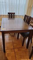 Photo of wood dining table showing entire surface and legs in a room with parquet flooring and window curtains.