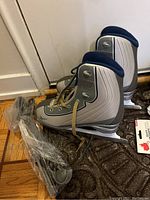 Pair of ladies Reebok ice skates on a floor with attached blades and skate guards wrapped in plastic.