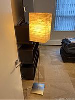 Floor lamp turned on showing light through textured rectangular paper shade on metal base