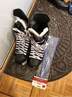 Pair of black and red CCM JetSpeed Custom 04 ice hockey skates, size 9, laced up and standing on floor next to a door, along with blue skate guards in plastic packaging.