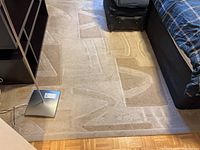 Beige area rug with geometric triangle and angular shapes pattern shown partially under furniture.