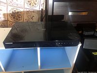 Front and top view of Samsung Blu-ray 3D player showing glossy black finish, control buttons, disc tray, and the Samsung logo.