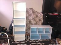 Both shelving units together: tall white shelving unit with five shelves and shorter five-cubby unit painted white with blue interiors.
