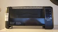 Front view of black Sunbeam electric heater showing metal mesh grille and control panel with touch buttons.