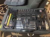 Photo showing the fully open Jobmate tool case with various tools arranged including hammer, tape measure, level, adjustable wrench, pliers, ratchets, sockets, screwdrivers, and Allen keys.