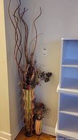 Large ribbed glass floor vase with tall twigs, berries, and pinecones next to smaller vase with twigs, showing overall look and contents.