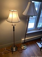 Photo of two retro metal floor lamps side by side, each with a beige lampshade, one fixed neck and one adjustable neck.
