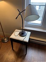 Table lamp with adjustable black metal neck and beige fabric shade on top of a small storage stool with a white cushioned lid.