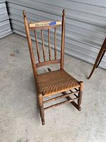 Front view of vintage child-sized wooden rocking chair showing woven seat, spindle backrest, and aged wood wear.